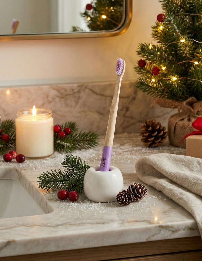 Bamboo toothbrush with a purple bristle head in a white holder on a bathroom counter with Christmas decorations.
