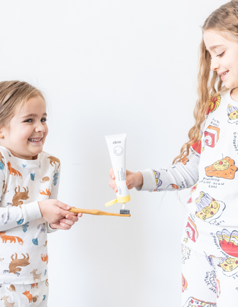 Two kids help each other brush their teeth using ELIMS Reflection toothpaste in pineapple orange mint. Combines natural ingredients like nano-hydroxyapatite, a natural mineral and fluoride alternative. Formulated with input from dentists to gently remineralize teeth and keep your mouth fresh all day or night. Foodie friend approved!